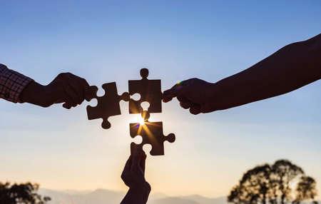 hands holding piece of blank jigsaw puzzle at sunset backgroundの写真素材