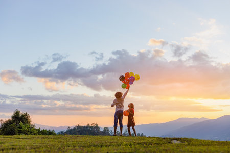 Two cute little girls playing on mountain park with air balloons at sunset. Best friends.の写真素材