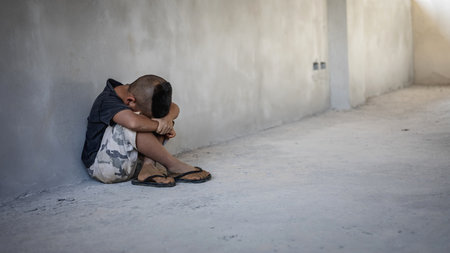 Homeless sad little child sitting alone on floor concrete wall backgroundの写真素材