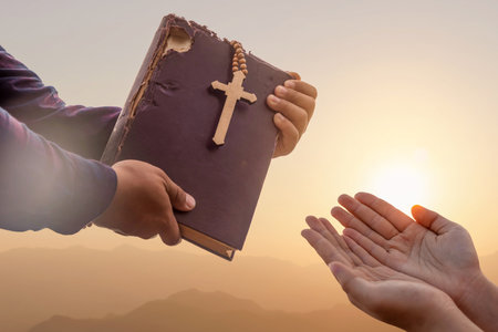 Close up father hand giving Bible and Cross legacy to young person at sunset background, Religion and Hope Concept.の写真素材