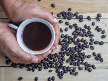 roasted coffee beans and hands holding coffee cup on wooden tableの写真素材