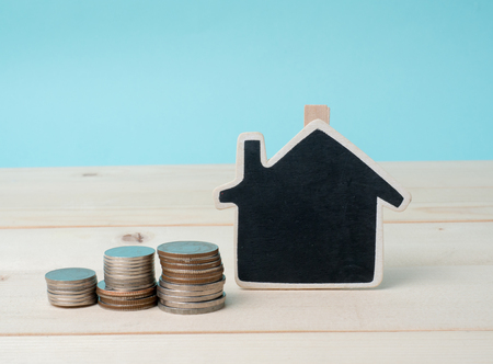 coin stack with house model, savings plans for housing blue background, financial concept. House and coins on table.Concept for property ladder, mortgage and real estate investment.の写真素材