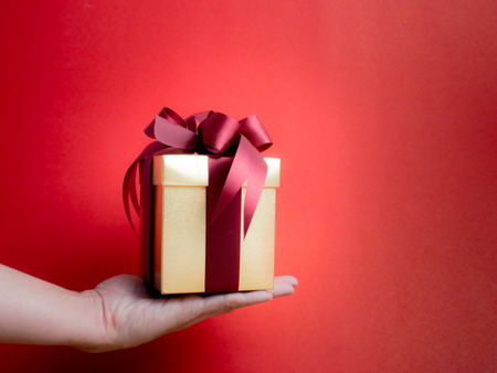 Valentine festival , New year Gold gift box with red ribbon. Red background for create idea copy space.hand holding gift boxの写真素材