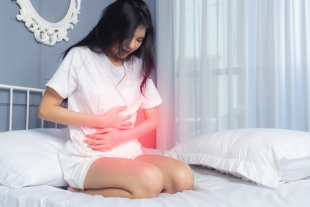 Young woman suffering from abdominal pain while sitting on white  bed at home. Do not oversleep againの写真素材
