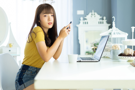 Happy asian beautiful woman working on a laptop sitting on the table  in the house.Morning she dress sweater and work at home .の写真素材