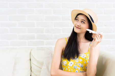 Asian woman's hand flying toy plane .Beautiful young woman smiling  planning  vacation summer trip.she think  and sitting sofa on brick background.の写真素材