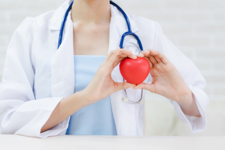 Young woman doctor holding a red heart, standing on brick wall backgroundの写真素材