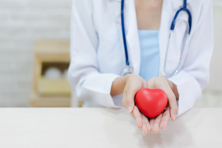 Young woman doctor holding a red heart, standing on brick wall backgroundの写真素材