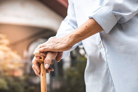 Close up of elderly hands in wrinkles holding walking stick.elderly old man with walking stick stand on footpath sidewalk crossing.の写真素材
