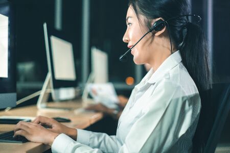 Asian confidence operator woman agent with headsets working in a call center at night Environment...