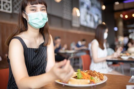 Asian woman sitting separated in restaurant eating food .keep social distance for protect infection from coronavirus covid-19, restaurant and social distancing concept.の写真素材