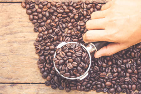 Close up hand and stainless scoop with coffee beans scattered beans on dark wood background.の写真素材