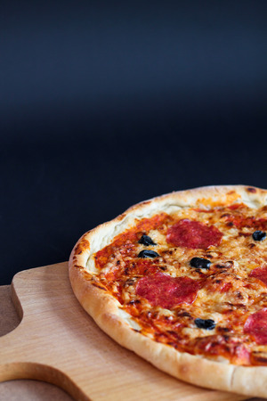 Delicious pizza pepperoni with black olives on cutting boardの写真素材