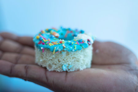 Donut with colorful sprinkles on the hand isolated on blue backgroundの写真素材