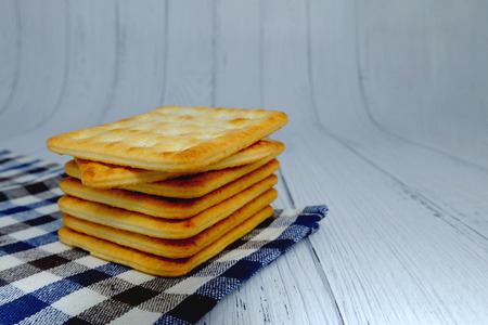 Cracker squares stacked, Cracker squares stacked on plaid fabric, Cracker squares stacked on white wood backgroundの写真素材