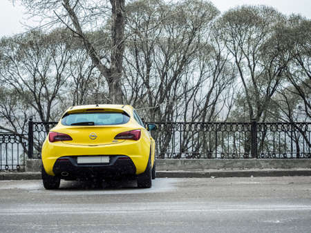 Yellow opel astra parked near the iron fence. It's snowing outside. Trees on a backgroundのeditorial素材