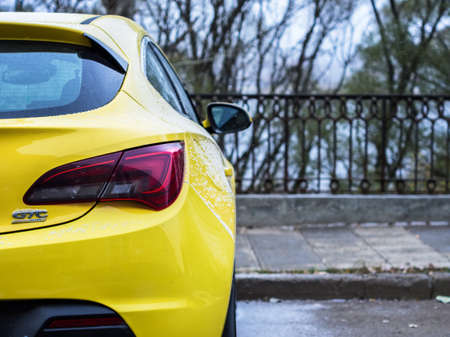 Yellow opel astra parked near the iron fence. Autumn, november. It's snowing outside. Trees on a backgroundのeditorial素材