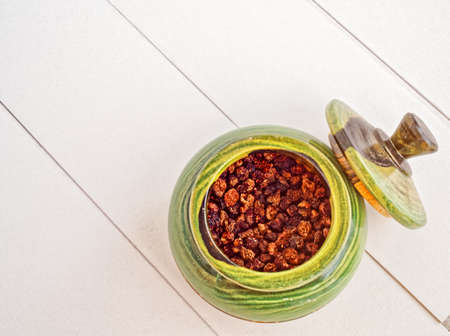 Dried raspberries in a green ceramic pot with a lid on a background of white boardsの写真素材