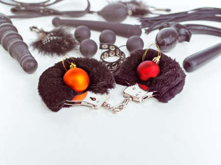 Red and golden Christmas balls are in furry handcuffs. Behind them are various sex toys. Below there is an empty space for textの写真素材