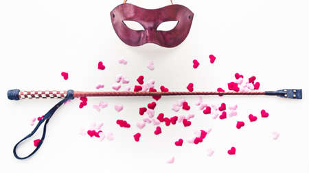 The Venetian mask and whip are on a light background with pink and red heart made of cloth. Romantic background for goods from a sex shop, costume party, Valentine's Dayの写真素材