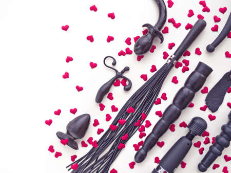 Various rubber sex toys (dildo, butt plug, whip, vibrator and other) are arranged on a white background with red hearts. Romantic background for goods from a sex shop or Valentine's Dayの写真素材