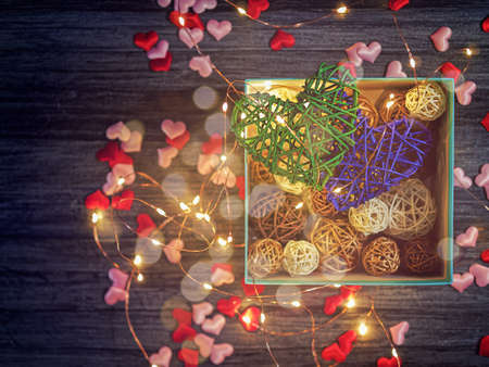 Two wicker hearts together with a luminous garland. Around are scattered small hearts of cloth....
