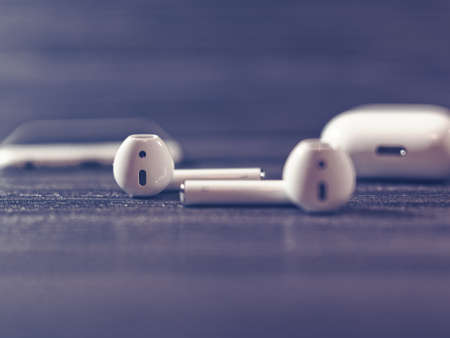 Moscow, Russia - December 19, 2017: White iPhone, wireless AirPods headphones, a box for recharging headphones are on a dark wooden background. Products developed by Apple Inc.のeditorial素材