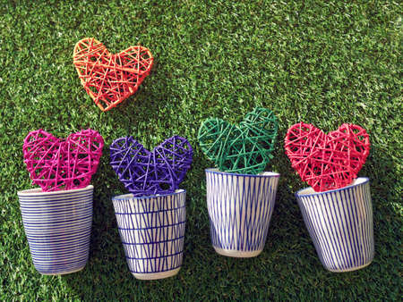 Multicolored wicker hearts are in the porcelain cups against the background of the green grass. Romantic background for a happy Valentine's Day, engagement or wedding invitationの写真素材