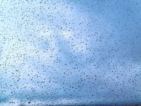 Raindrops on the window on the background of a formidable blue sky. Natural background for sad mood...