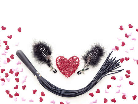 Red wicker heart and two nipple clamps with feathers (sex toy) are on a white background. Around...