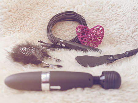Various sex toys (leather whip, nipple clamps, wand massager, slapstick) and a red wicker heart are on a fur background. Image in retro style to Valentine's Dayの写真素材