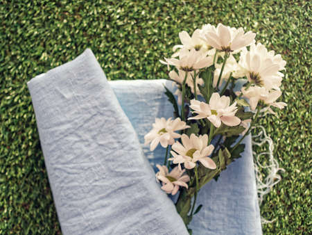 A bouquet of fresh white chamomile chrysanthemum is wrapped in a blue linen fabric with untreated edges. Spring green grass background.の写真素材