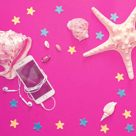 IPhone with connected headphones, starfish, seashells of different sizes are on an ultraviolet...