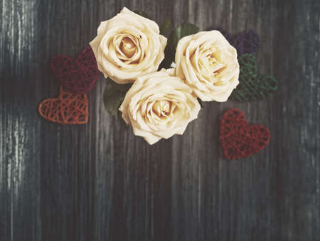 Three white roses and several wicker hearts are on a dark wooden background. View from above. Image in gloomy tonesの写真素材
