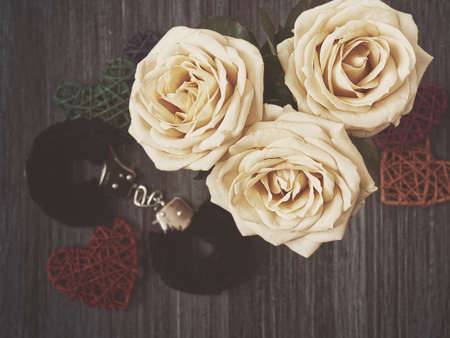 Three white roses, fur cuffs and a few wicker hearts are on a dark wooden background. View from above. Image in gloomy tonesの写真素材