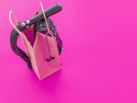 A leather whip and a collar with clamps are on a paper shopping bag. Background suitable for sex shop advertisingの写真素材