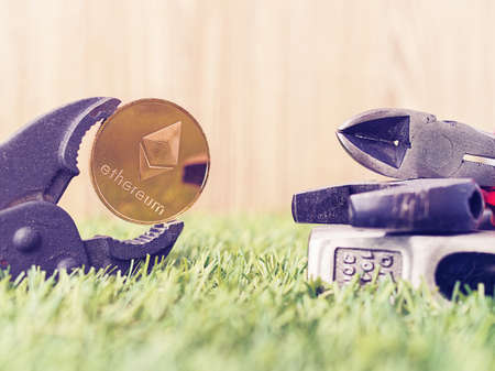 The coin of the crypto currency Ethereum is clamped in a wrench. There are other tools on the green...