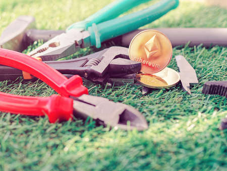 Coins of crypto currency Ethereum together with various tools for manual work are on the green grass. Image about earnings on the Internet and the real worldの写真素材
