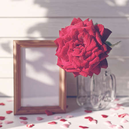 Romantic composition for Valentine's Day. A fresh red rose is near an empty wooden photo frame on a light wooden background. Decoration with figures in the form of hearts. Copy space.の写真素材