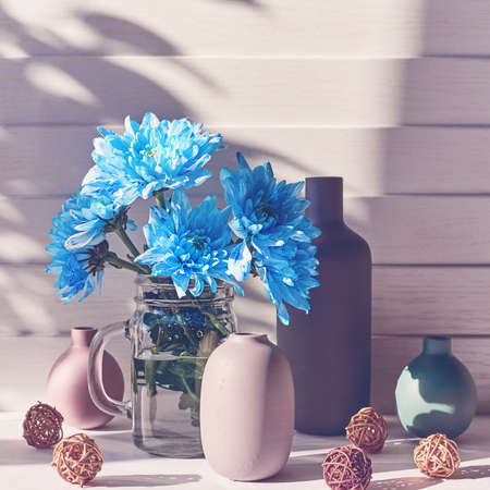 A bouquet of blue chrysanthemums or chamomiles is in a glass jar. Behind there are various...