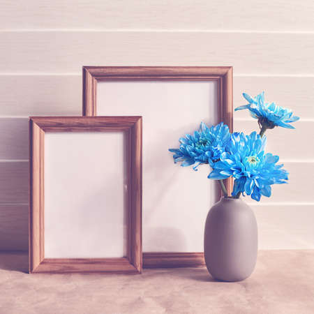 Blue chrysanthemums or chamomiles are in a gray vase. Behind there are two empty wooden frames. White wooden backgroundの写真素材