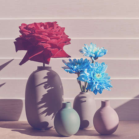 A fresh red rose with drops on the petals is in a large gray opaque vase. The bed is a smaller vase with a bouquet of blue chrysanthemums. There are two empty mini-vasesの写真素材