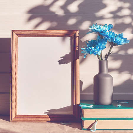 An empty wooden frame with a shadow of the trees on it. The distance is a gray vase with blue...