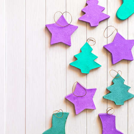 Green and purple Christmas toys made of paper are on a white wooden background. Flat lay, top view,...
