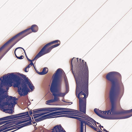 Different sex toys (fur handcuffs, leather whip, butt plug, spanking pad and other) are on a white wooden background. Idea for sex shop advertisingの写真素材