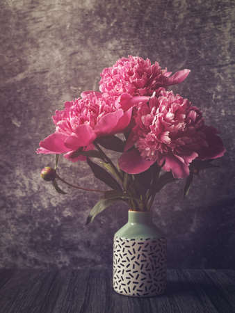 A bouquet of red and pink peonies in a vase with a pattern. Dark stone background.の写真素材