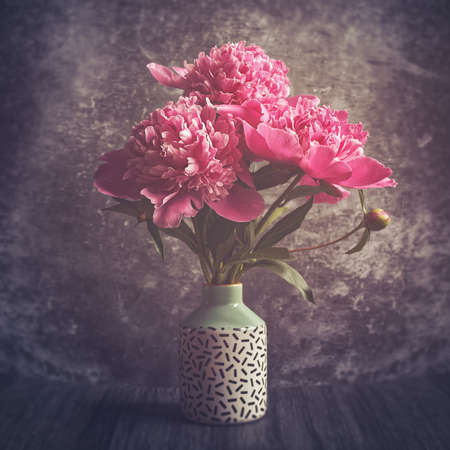 A bouquet of red and pink peonies in a vase with a pattern. Dark stone background.の写真素材