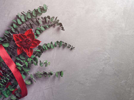 Flower composition. Red flower, red ribbon and eucalyptus are on a gray background. Flat lay, top view. Copy space.の写真素材