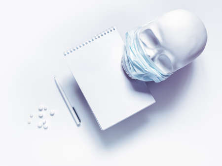 A protective mask is worn on the skull. Nearby is a notebook and pen. The concept of protection against viruses, bacteria. Prevention of airborne diseases. Health protection. Fkat lay. Copy space.の写真素材