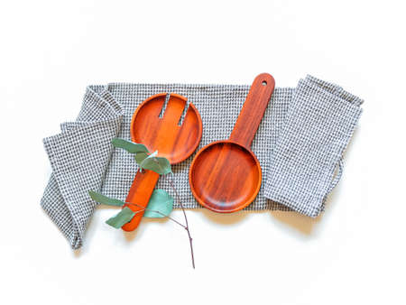 A wide wooden fork and a spoon for serving salad and a branch of eucalyptus are on a gray waffle towel on a white background. Kitchen concept. Top view. Flat lay.の写真素材